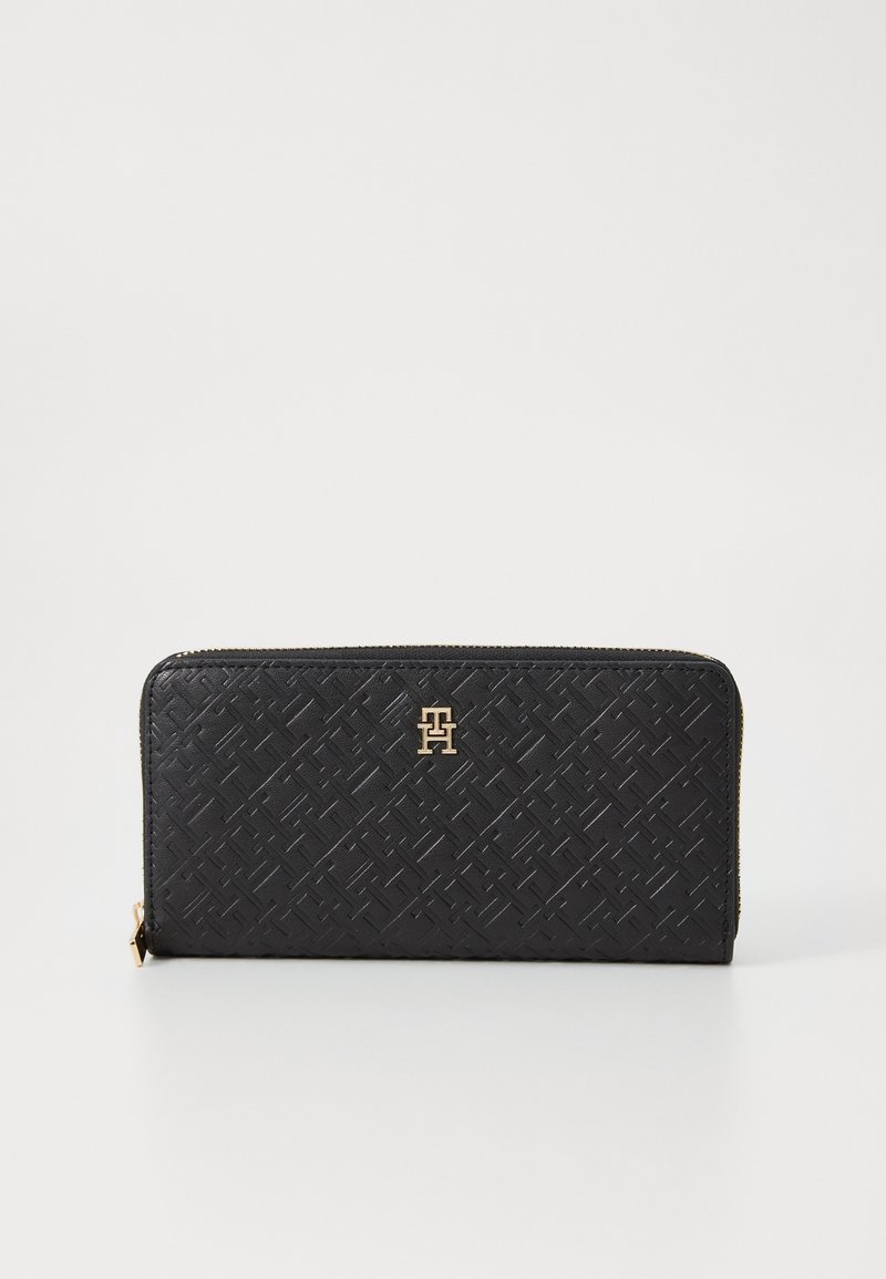 Melns maks, izgatavots no teksturēta materiāla ar austu rakstu, ar zelta piederumiem un logo priekšpusē, ar rāvējslēdzēja aizdari vienā pusē.