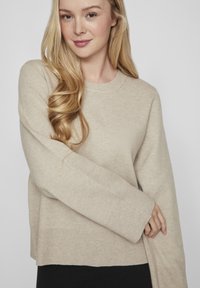 Bežinė megzta palaidinė su ilgomis rankovėmis, apvaliu kaklu ir laisvu siluetu. Savybės: ripsuoti rankogaliai ir apačia. Minkšta tekstūra, minimalistiškas dizainas.