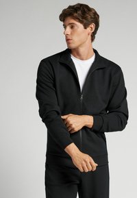 Svart zip-up sweatshirt i mjukt tyg med ståkrage, ribbad mudd och kontrasterande foder vid kragen.