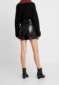 Černý pletený svetr s oranžovým límcem, doplněný lesklými černými šortkami z umělé kůže. Modelka má na sobě černé kotníkové boty.