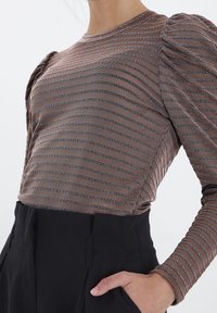 Brun randig långärmad topp med puffärmar. Tyget har växlande svarta och vita mönster, kombinerat med svarta högmidjade byxor.