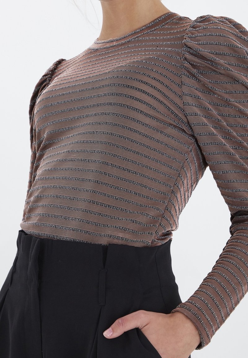 Brun randig långärmad topp med puffärmar. Tyget har växlande svarta och vita mönster, kombinerat med svarta högmidjade byxor.