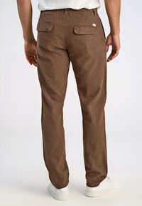Brązowe, lekko teksturowane spodnie z bocznymi i tylnymi kieszeniami, elastycznym pasem i zwężanymi nogawkami, w połączeniu z białymi butami.