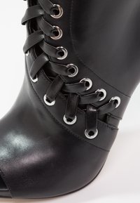Bottine en cuir noir avec un design à lacets sur le devant passant à travers des œillets en métal argenté.