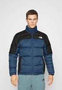 Giacca imbottita di colore blu navy con dettagli neri, colletto alto, chiusura con zip, polsini a costine e tasche laterali con un design in tessuto testurizzato.