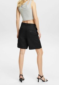 Zwarte linnen shorts met omgeslagen zoom en twee achterzakken, gecombineerd met een grijze cropped tanktop. De look wordt compleet gemaakt met zwarte hoge hakken.
