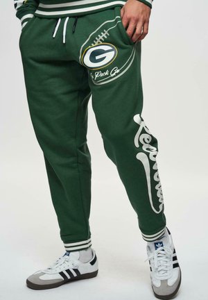 Green sweatpants made of cotton, featuring a football graphic and white lettering on the leg. Ribbed cuffs and drawstring waist detail.