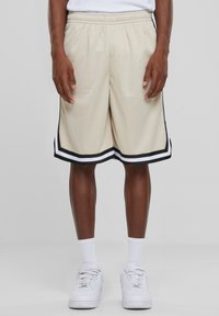 Beige mesh shorts med elastisk talje, med en sort og hvid stribet kant. Båret med hvide sko og sokker.