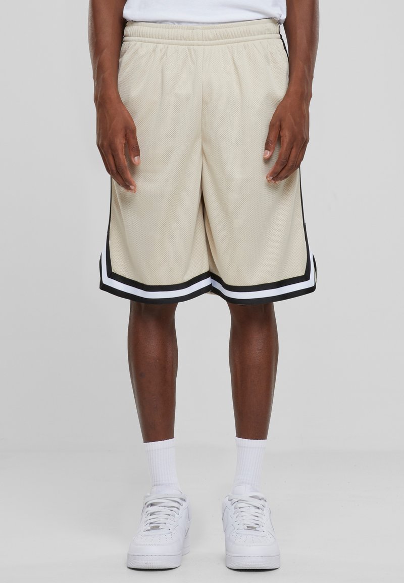 Beige mesh shorts med elastisk talje, med en sort og hvid stribet kant. Båret med hvide sko og sokker.