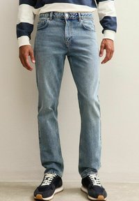 Jeans de mezclilla azul claro con corte recto, diseño de cinco bolsillos y cierre de botón. Llevados con zapatillas negras de cordones blancos.