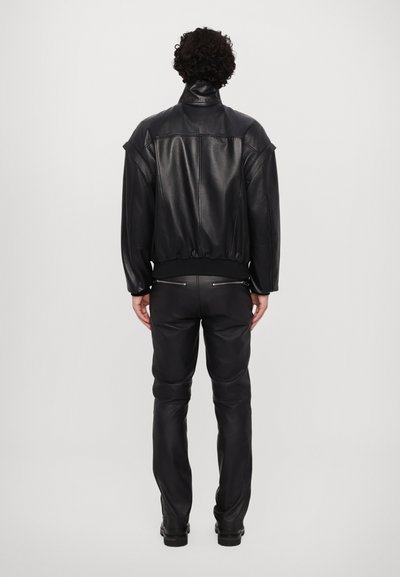 Black leather bomber jacket with ribbed cuffs and hem, featuring shoulder seams, and paired with black leather pants and black boots.