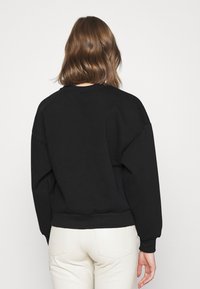 Svart oversized sweatshirt med rundad hals och ribbade ärmar. Tyget verkar mjukt med en subtil textur. Bärs tillsammans med byxor i krämfärg.