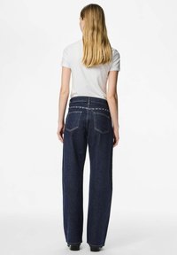 Temno modre široke kavbojke z visokim pasom in žepki na zadnji strani, z diskretnim šivanjem in okrasnimi kovinskimi dodatki.