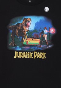 T-shirt en coton noir avec un graphique vibrant d'un T-rex et d'une figure humaine, avec le texte "Jurassic Park" en jaune en bas.