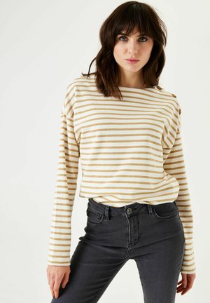 T-shirt à manches longues rayé en crème et or, avec une coupe décontractée, un col rond et des boutons aux épaules, associé à un jean gris foncé.