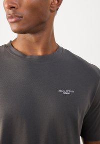 Mörkgrå bomullströja med korta ärmar och rund halsringning. Har en vit logotyp med "Marc O'Polo DENIM" på vänster bröst.