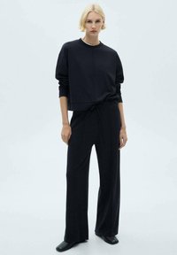 Completo a due pezzi in nero: felpa corta con polsini a coste e pantaloni ampi a vita alta, entrambi in tessuto morbido. Design semplice e minimalista.