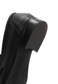 Czarna skórzana shoe z zaokrąglonym czubkiem i niskim, solidnym drewnianym obcasem. Materiał ma teksturowane wykończenie, a podeszwa jest gładka.