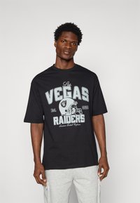 Juoda marškinėliai su „Las Vegas Raiders“ grafika pilka ir mėlyna spalvomis, su futbolo šalmu iliustracija. Trumpomis rankovėmis, laisvas kirpimas.