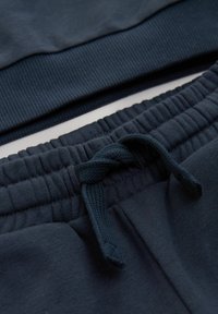 Sweatshirt et pantalon de jogging en coton bleu marine avec des poignets côtelés, présentant un cordon de serrage et un tissu texturé pour le confort et l'ajustement.