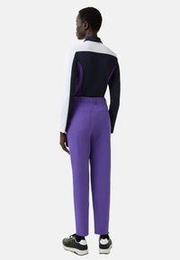 Dvoubarevný sportovní outfit zahrnující tmavě modrý a bílý dlouhý rukáv s fialovými akcenty a fialové kalhoty s vysokým pasem. Součástí jsou černé tenisky.