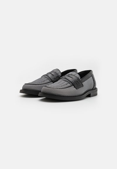 Schwarz und grau gemusterte Slipper mit einem glatten schwarzen Lederakzent am Riemen. Flache Sohle und abgerundete Zehenform. Beschichtetes Textil-Obermaterial.