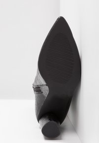 Chaussure noire à talon haut avec une tige texturée à motif crocodile, bout pointu et semelle en caoutchouc rainurée. Dotée d'un talon fin et cylindrique.