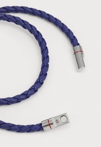 Filo in pelle intrecciato di colore viola con connettori metallici argentati caratterizzati da accenti rossi. La texture è liscia con una finitura lucida.