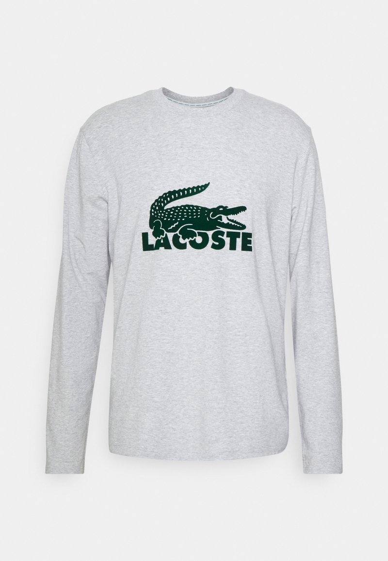 T-shirt gris à manches longues avec un logo crocodile vert et le texte "LACOSTE" en caractères gras en dessous du logo. Matière en coton doux.