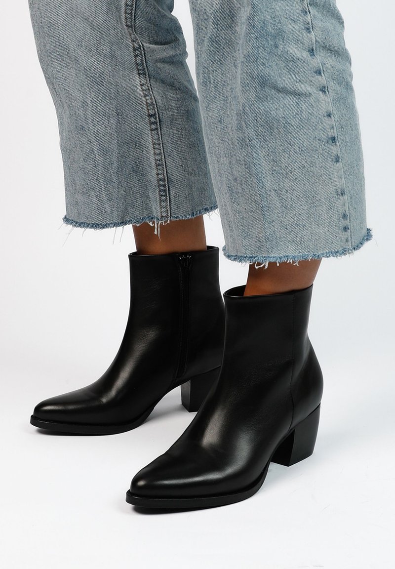 Stivali alla caviglia in pelle nera con punta allungata, tacco squadrato e zip laterale. Indossati con jeans azzurri con orlo sfrangiato.