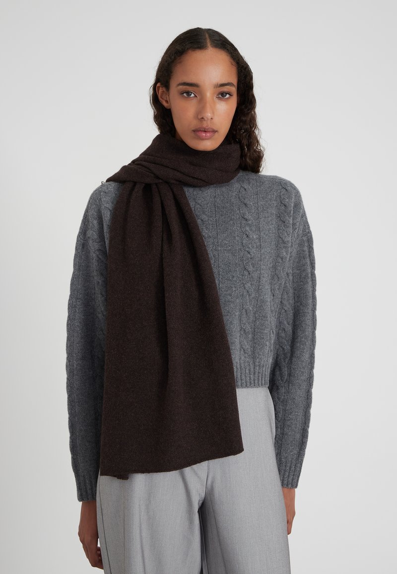 Sciarpa di lana marrone scuro avvolta attorno al collo, abbinata a un maglione grigio chiaro a trecce, che mette in evidenza texture morbide e colori a contrasto.