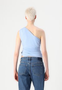 Lichtblauw, een-schoudertop met geplooid materiaal aan de zijkant, gecombineerd met hoge blue denim jeans met achterzakken.