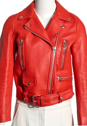Veste courte de motard en cuir rouge avec fermetures éclair argentées, détails de boutons et ceinture assortie, portée sur un pantalon blanc sur un mannequin.