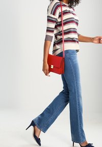 Red crossbody bag with gold hardware, striped knit top in cream, navy, and burgundy, paired with light blue flared jeans and navy heels.