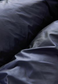 Tengerészkék selyem anyag, puha fényességgel, gyűrött textúrával és sima felülettel. Két átfedő rész látható.