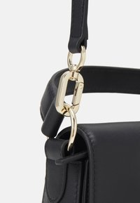 Correa de bolso de cuero negro con herrajes dorados, que presenta un cierre de clip y una textura suave, mostrando un diseño minimalista.