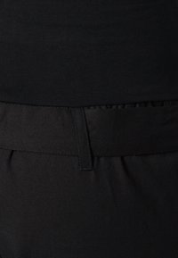 Pantalones de tela negra con una textura suave, que presentan una cinturilla y detalles de costura, mostrados de perfil.