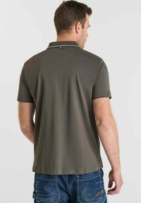 Polo de color verde oliva con una textura suave, mangas cortas y acentos blancos en el collar. La vista trasera muestra un corte clásico.