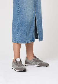 Grey sneakers featuring a mix of smooth and fuzzy textures, lace-up design, and a white sole, paired with a denim skirt with a front slit.