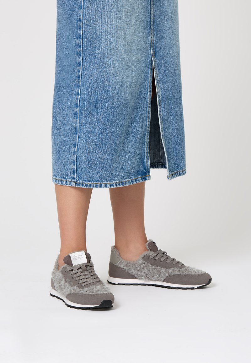 Grey sneakers featuring a mix of smooth and fuzzy textures, lace-up design, and a white sole, paired with a denim skirt with a front slit.