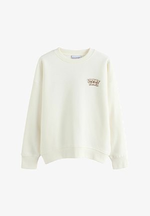 Eriti hele beež tooniga pikkade varrukatega ümara kaelusega dressipluus, millel on soonilised mansetid ja alaäär, ning mille vasakul rinnal on väike pruun "Looney Tunes" tekstilogoga märgistus.