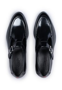 Schwarze Lacklederschuhe mit runder Spitze, ausgeschnittenen Seiten und verstellbarem Knöchelriemen mit Schnalle. Texturiertes Innenfutter.
