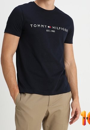 T-shirt bleu marine à manches courtes en coton, présentant un logo blanc avec des accents rouges et bleus. Encolure ronde et coupe standard.