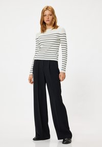 Witte geribde trui met zwarte strepen, gecombineerd met zwarte high-waisted broek met wijde pijpen. Beide kledingstukken hebben een gladde textuur.