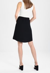 Jupe noire, longueur genoux avec une taille élastique, en tissu lisse. Associée à des chaussures noires à talons et un débardeur blanc ajusté.