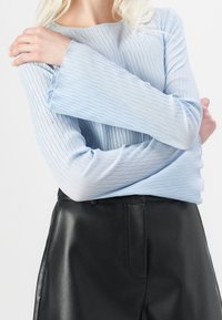 Světle modrý top s dlouhým rukávem a texturovaným plisovaným designem, doplněný černými koženými kalhotami. Rukávy mají mírné rozšíření.