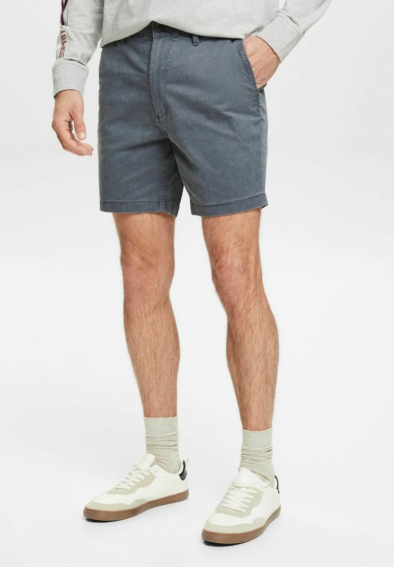 Grå bomulds shorts med lige snit og opsmøget kant, parret med hvide sneakers og lysegrå sokker. Enkel design og afslappet pasform.
