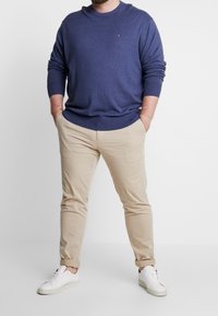 Maglione a maglia blu navy, chinos beige e sneakers bianche. Il maglione presenta un collo a giro e polsini a coste; i pantaloni sono slim-fit con orli arrotolati.