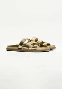 Gold sandals featuring multiple crossed straps and a flat sole. The material has a metallic finish, providing a smooth texture.
