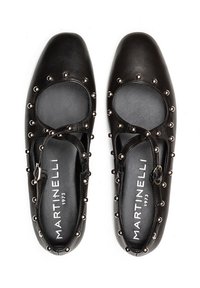 Zapatos de cuero negros con puntera redondeada, que presentan cortes circulares y acentos de tachuelas metálicas a lo largo de los bordes. Incluye una correa ajustable.